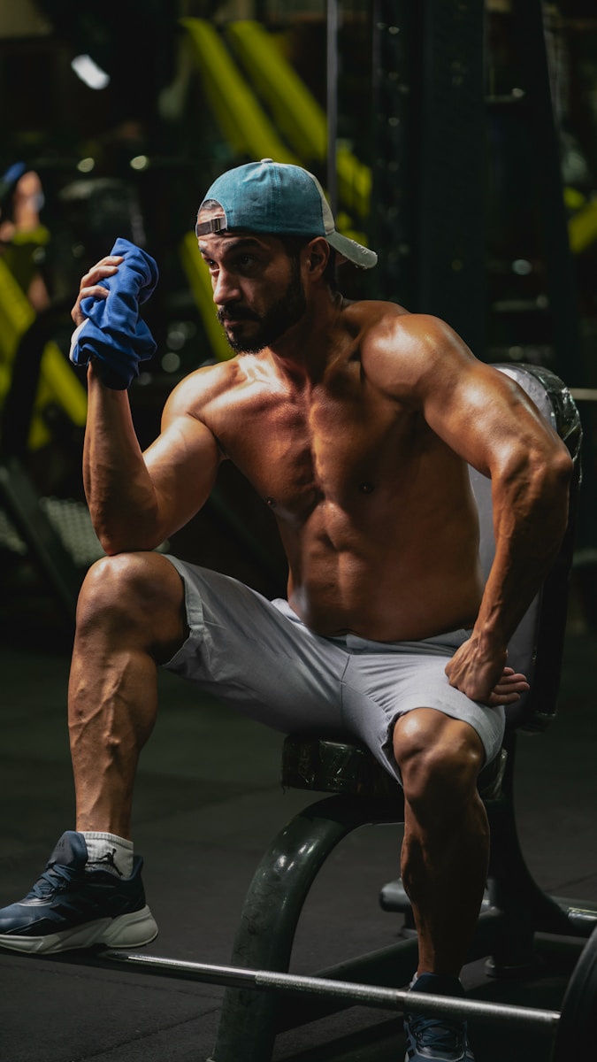 Photo by Mehran Biabani a shirtless man sitting on a bench in a gym